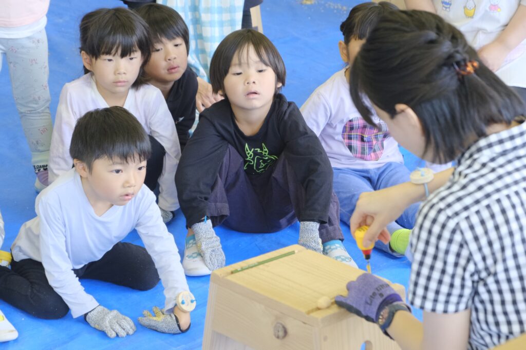 つまみを付ける穴あけの説明。真剣に見入る子ども達
