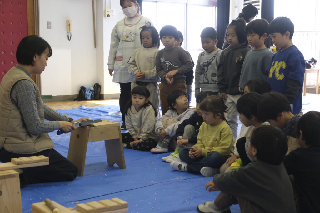 ノコギリの説明をきく子どもたち